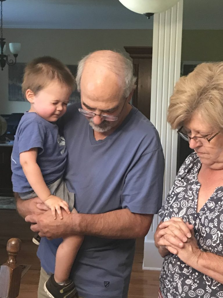 How to help your kids fall in love with prayer blog post - picture of two grandparents praying. The grandfather is holding a young child.